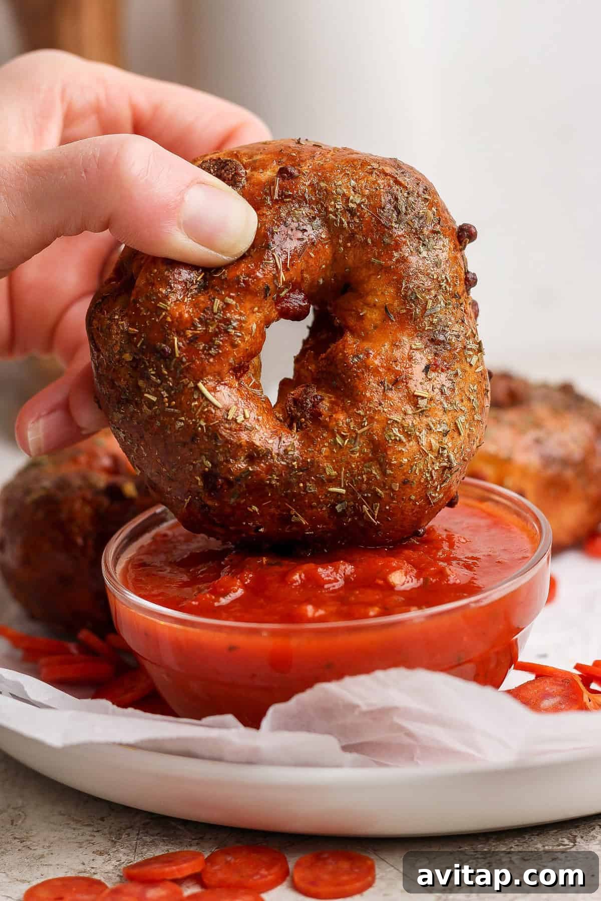 Hand dipping a pizza protein bagel into a bowl of marinara sauce