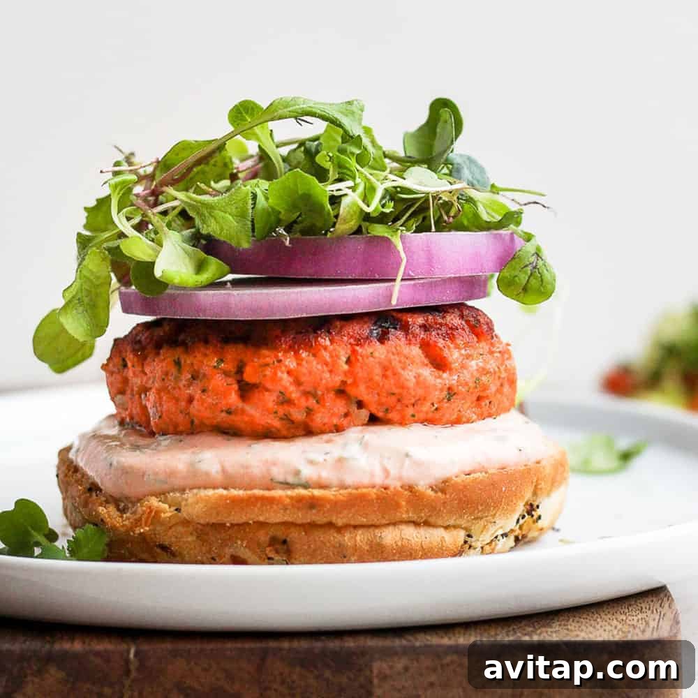 Delicious salmon burgers served with arugula and red onion on a white plate.