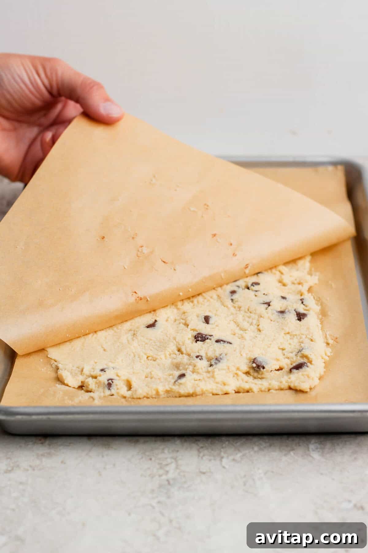 pressing cottage cheese cookie dough flat with parchment paper on a baking sheet