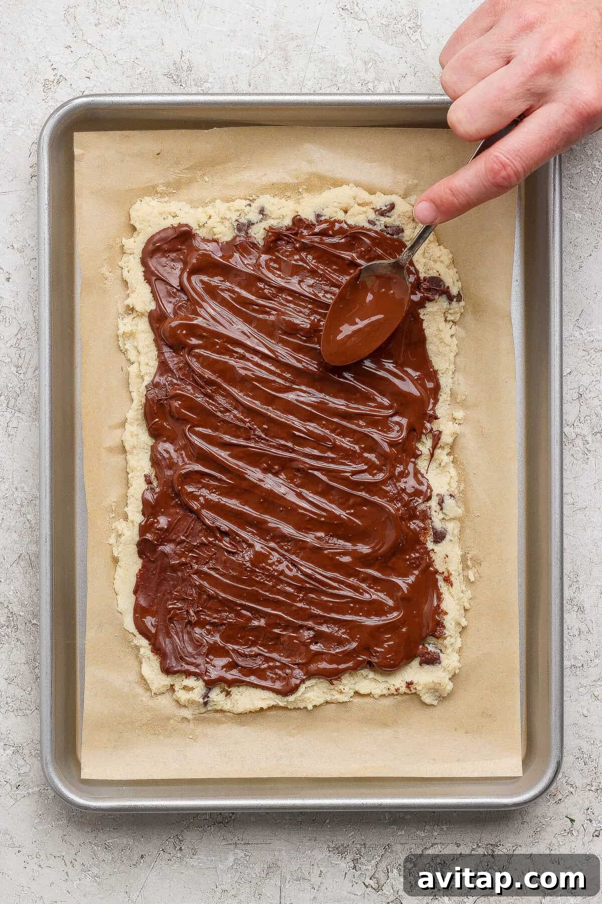 spreading melted chocolate over cottage cheese cookie dough bark with a spoon
