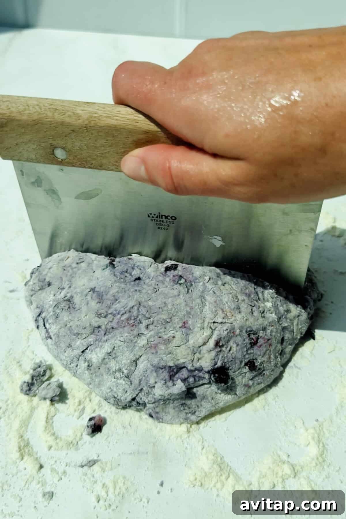 cutting blueberry biscuit dough on a floured surface with a dough scraper