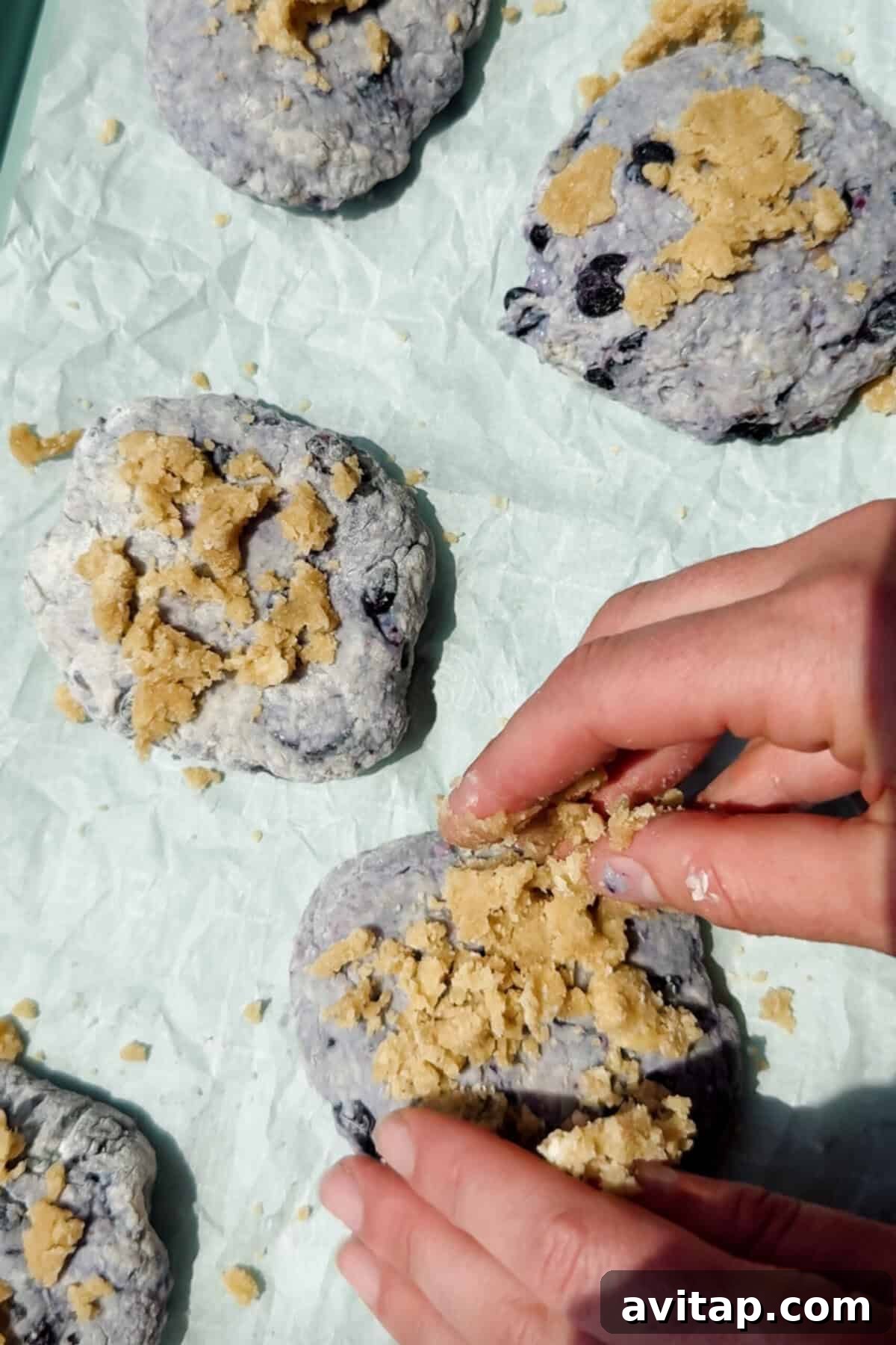 hand sprinkling streusel topping onto unbaked blueberry cottage cheese biscuits on parchment paper