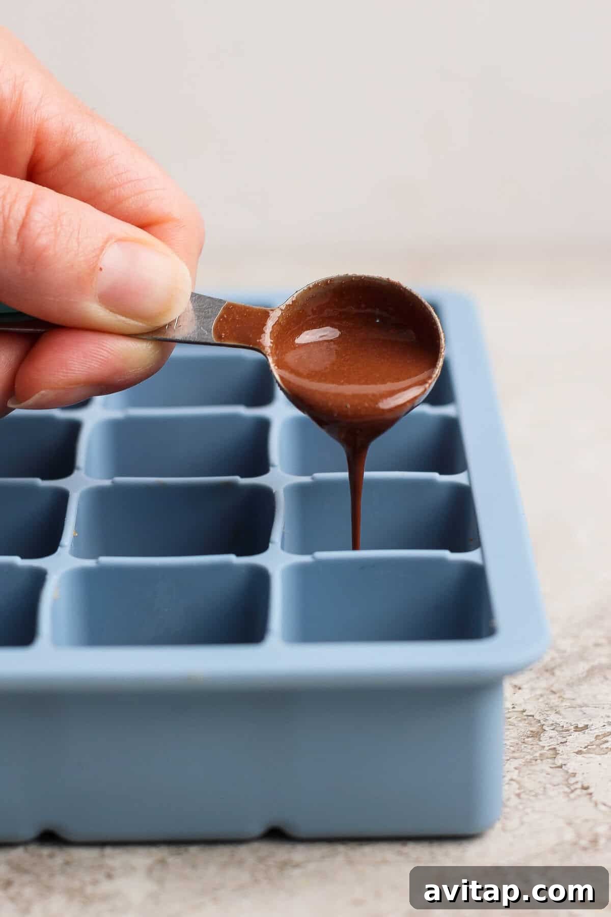 pouring melted peppermint chocolate over protein bite base in a silicone tray