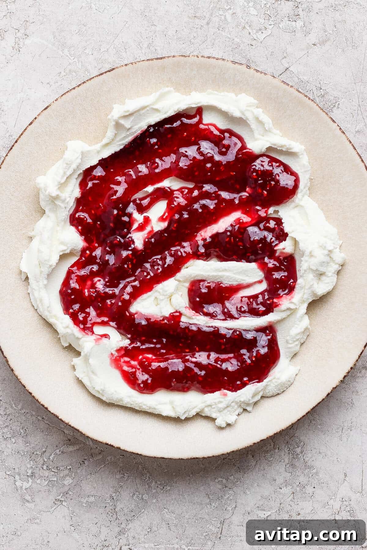 raspberry jam swirled over spread goat cheese on a plate