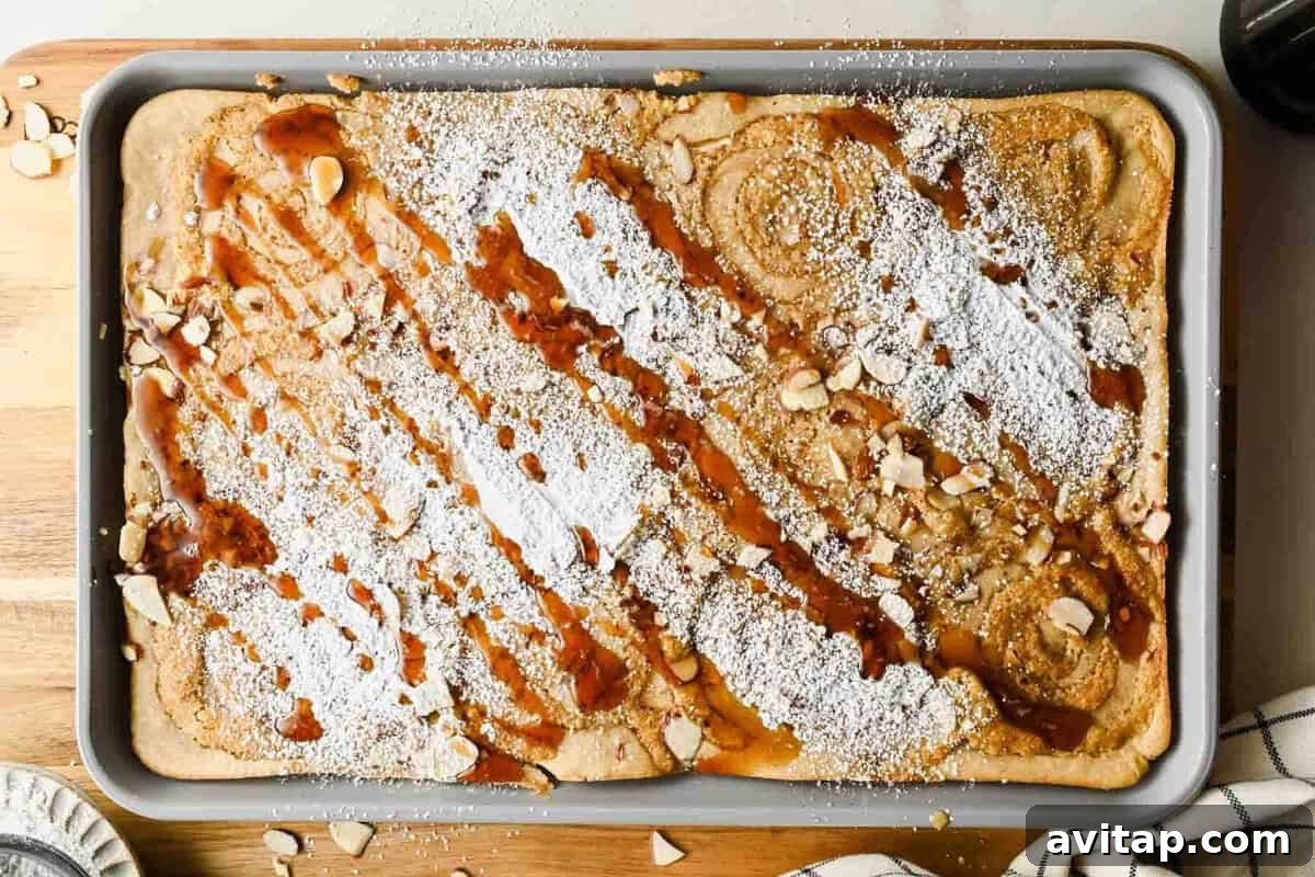 Baked sheet pan almond croissant pancakes dusted with powdered sugar and drizzled with maple syrup.