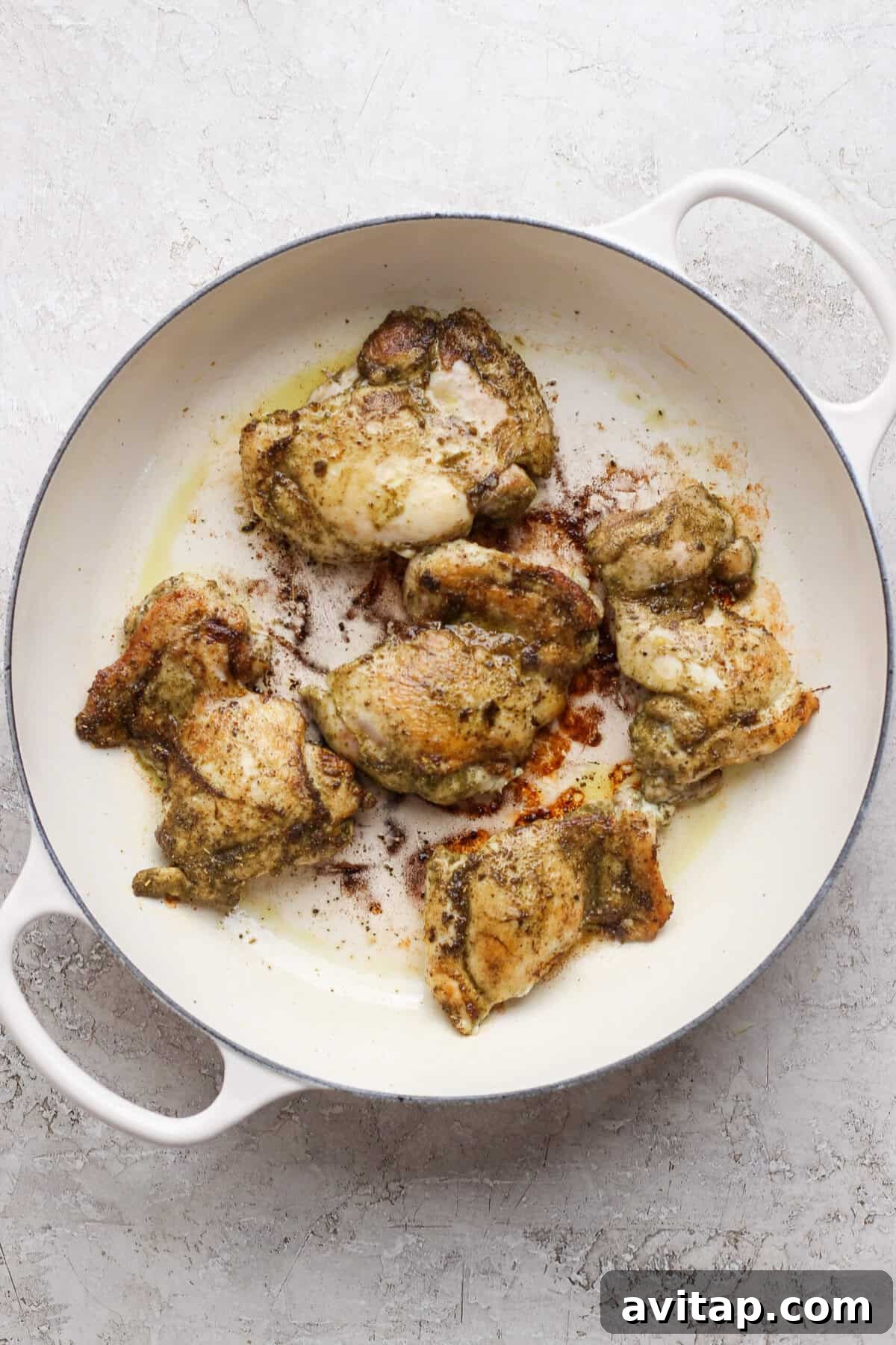Chicken thighs seared until golden brown in a white skillet.