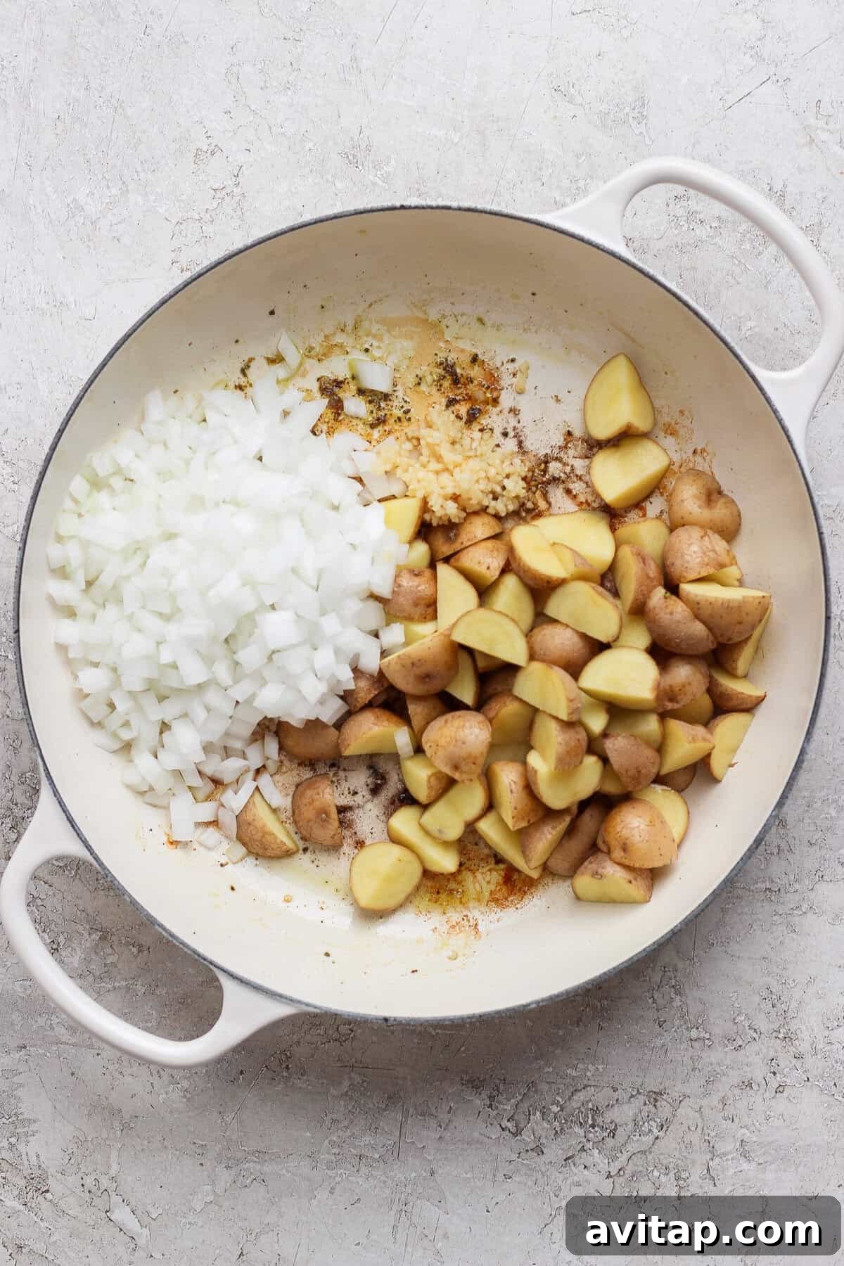 Diced white onion, minced garlic, and quartered baby potatoes in a white skillet.