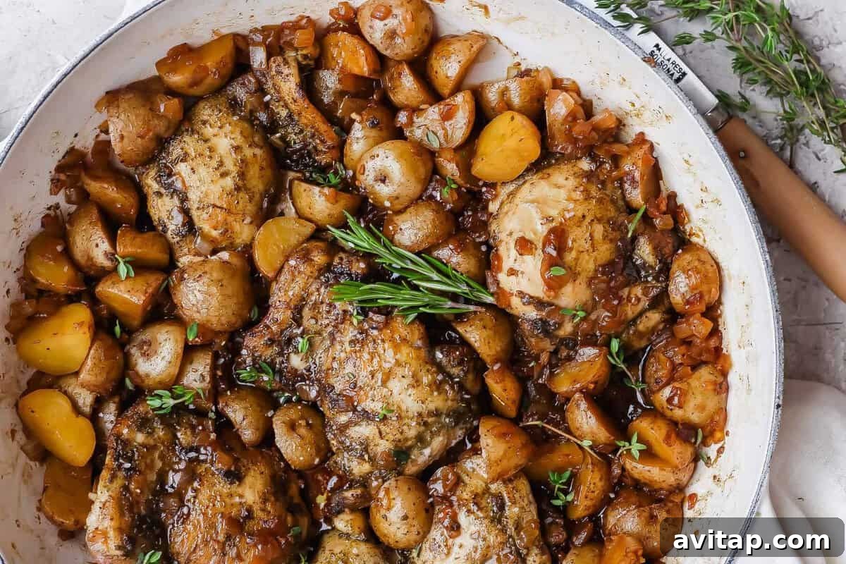 Apple cider chicken thighs nestled with baby potatoes and onion in a glossy skillet sauce.