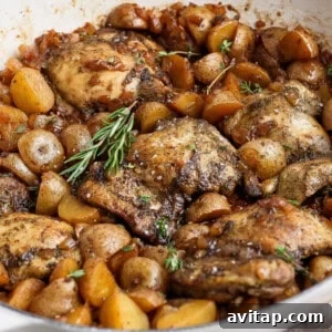 Saucy apple cider chicken thighs with golden baby potatoes, onion, and fresh rosemary in a white skillet.