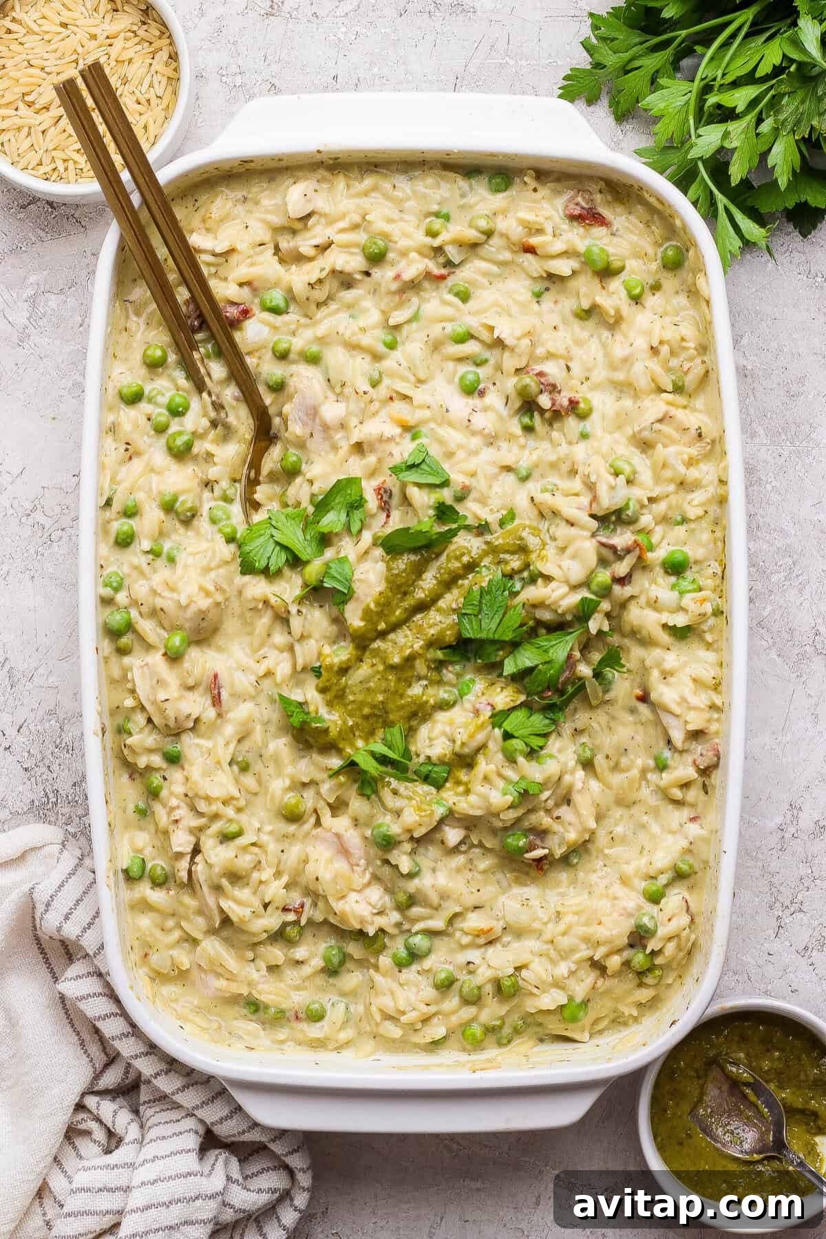Finished creamy chicken pesto orzo casserole garnished with pesto and fresh parsley.