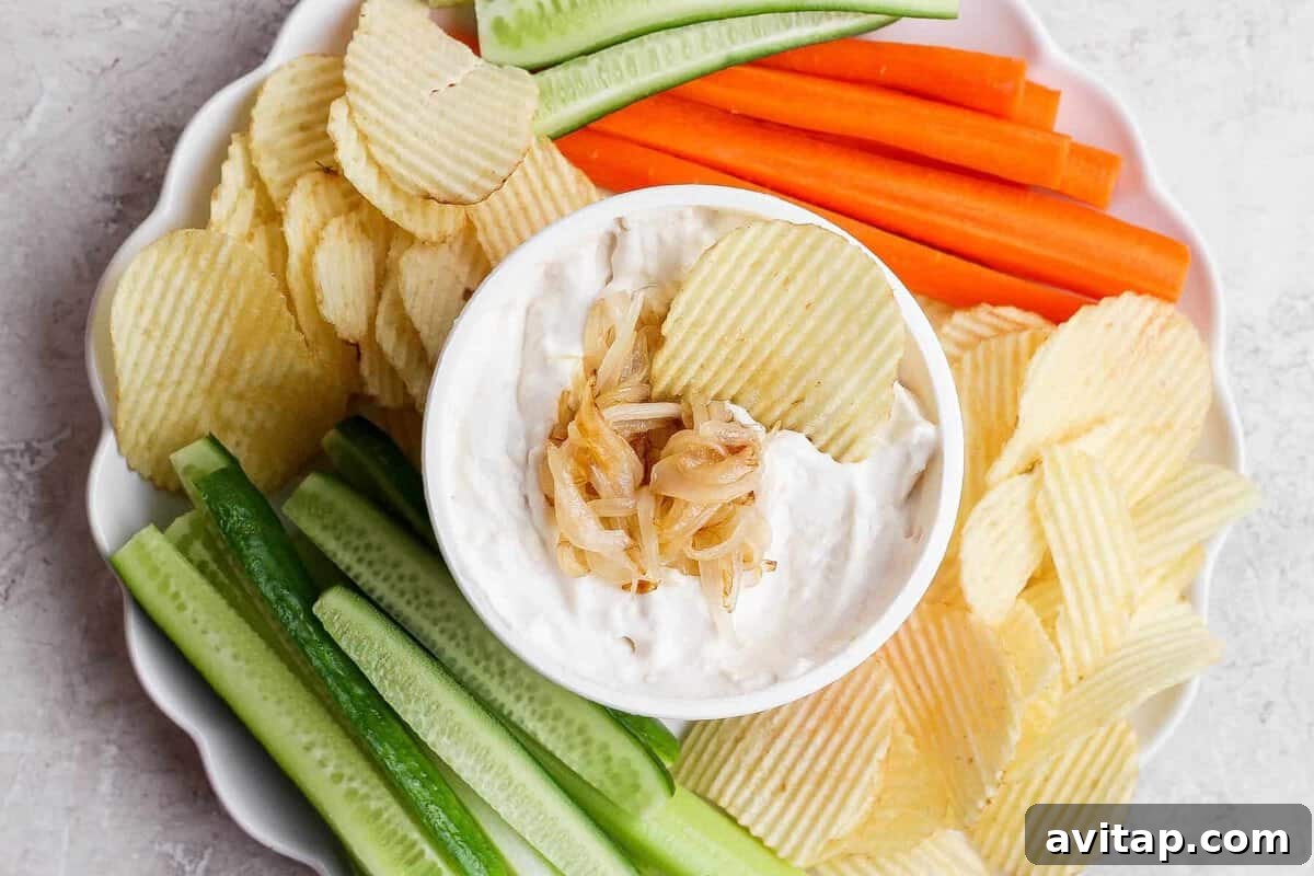 Overhead view of cottage cheese French onion dip surrounded by ridged potato chips, carrots, and celery on a serving platter.