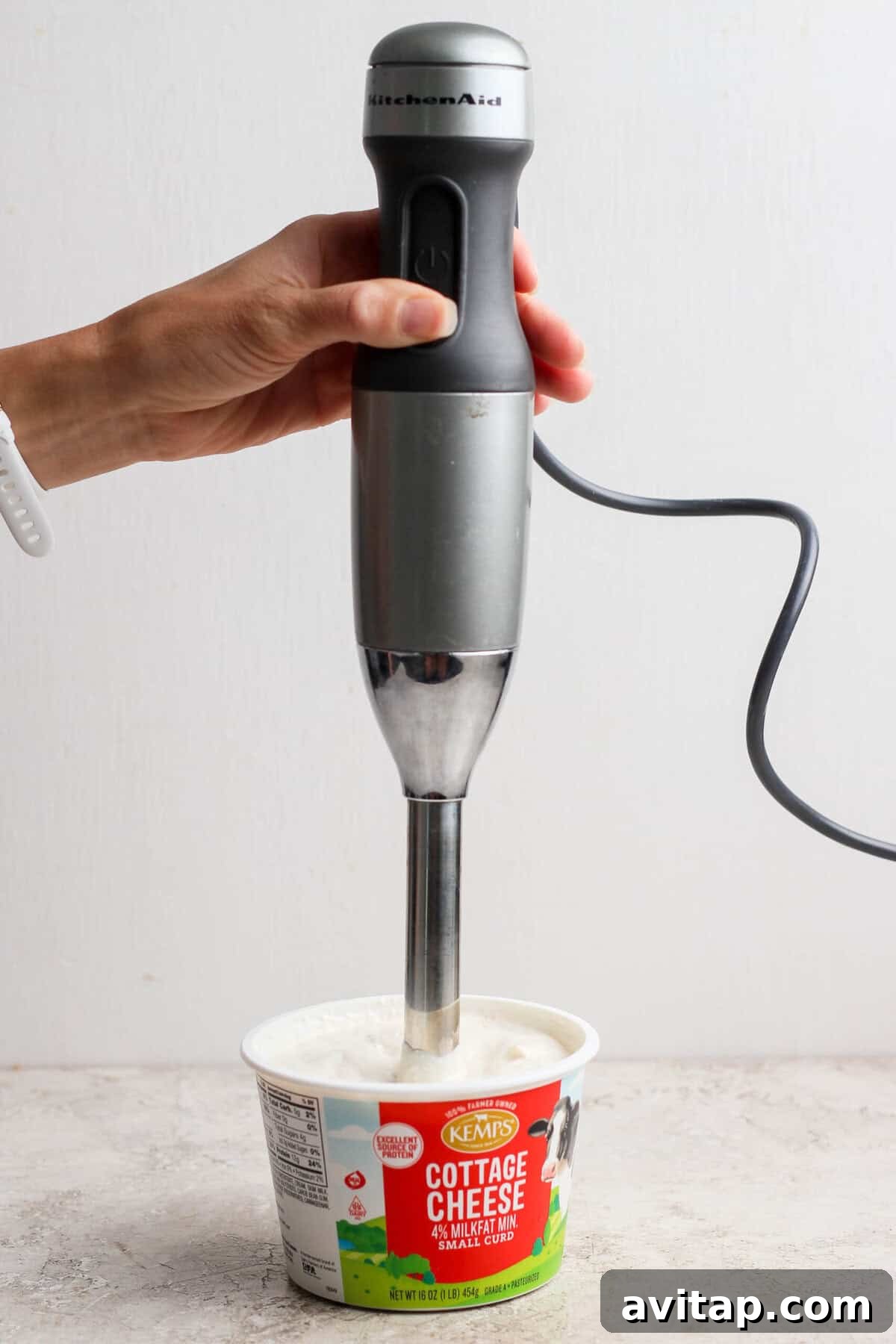 An immersion blender blending cottage cheese dip directly in the cottage cheese container.