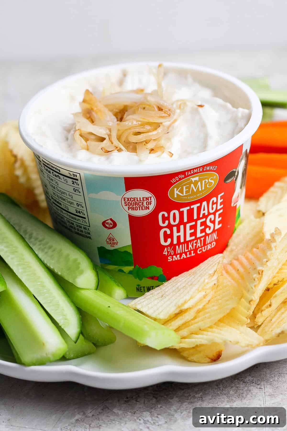 Finished cottage cheese French onion dip topped with golden onions and served in the cottage cheese container with potato chips and celery.