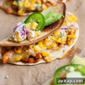 Close-up of a crispy baked chicken taco filled with creamy street corn salad and topped with avocado and jalapeño.