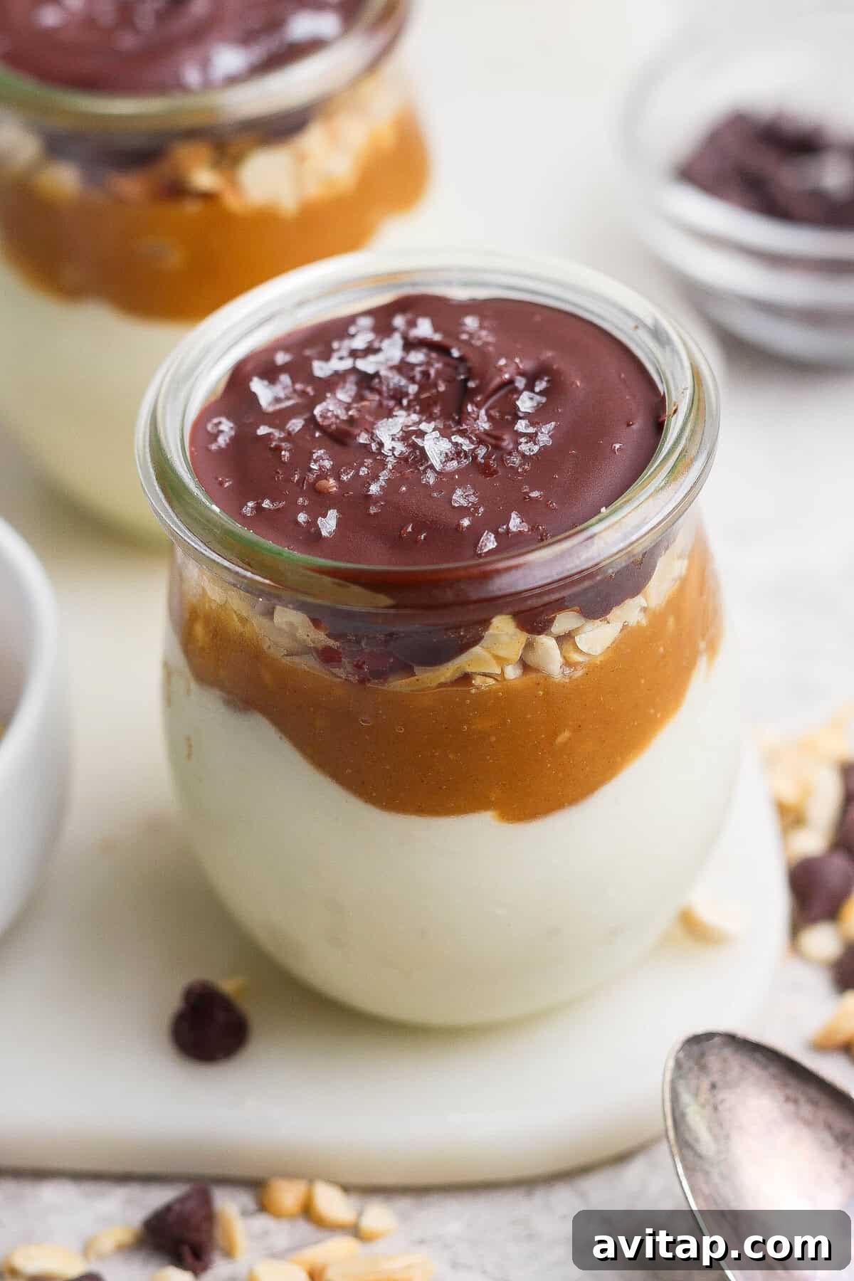 Individual Snickers cheesecake cup layered with blended cottage cheese, maple peanut butter, salted peanuts, and a glossy chocolate shell.
