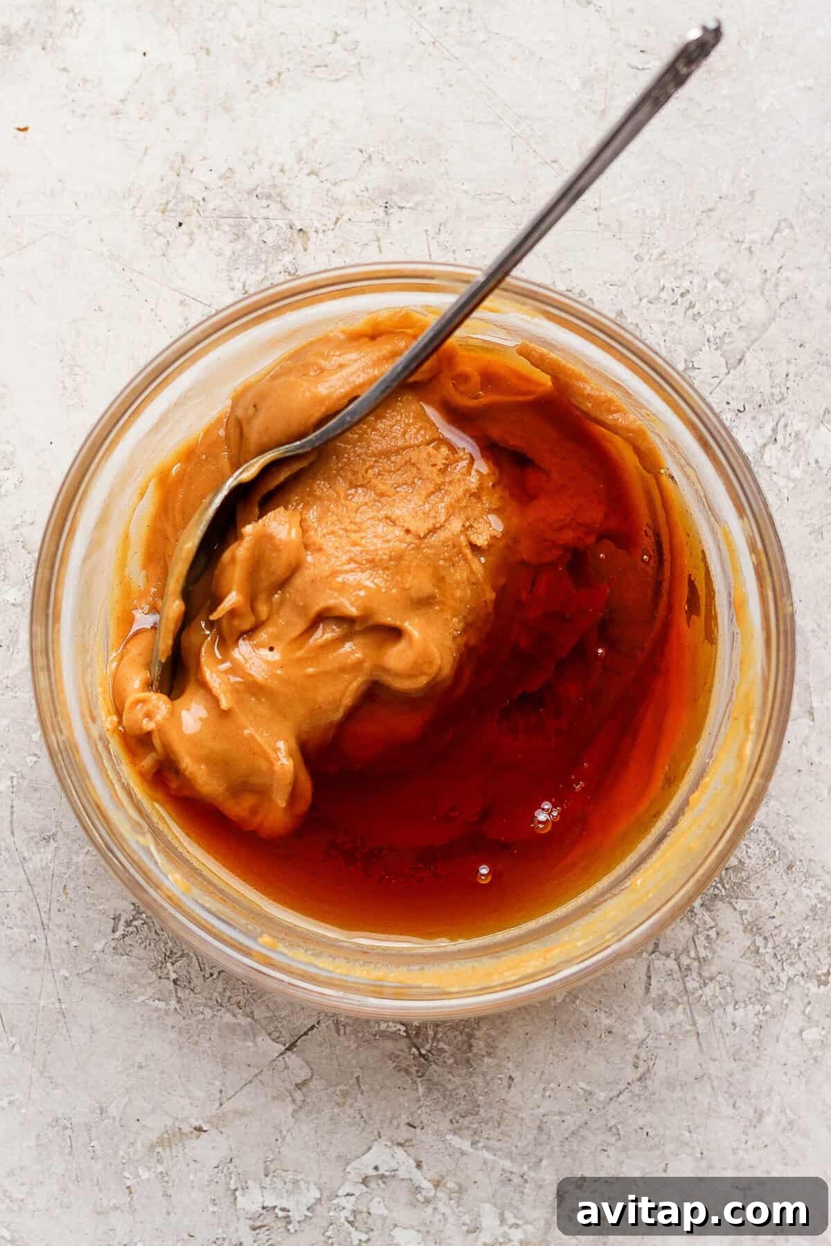 Creamy peanut butter and maple syrup being stirred together in a small glass bowl.