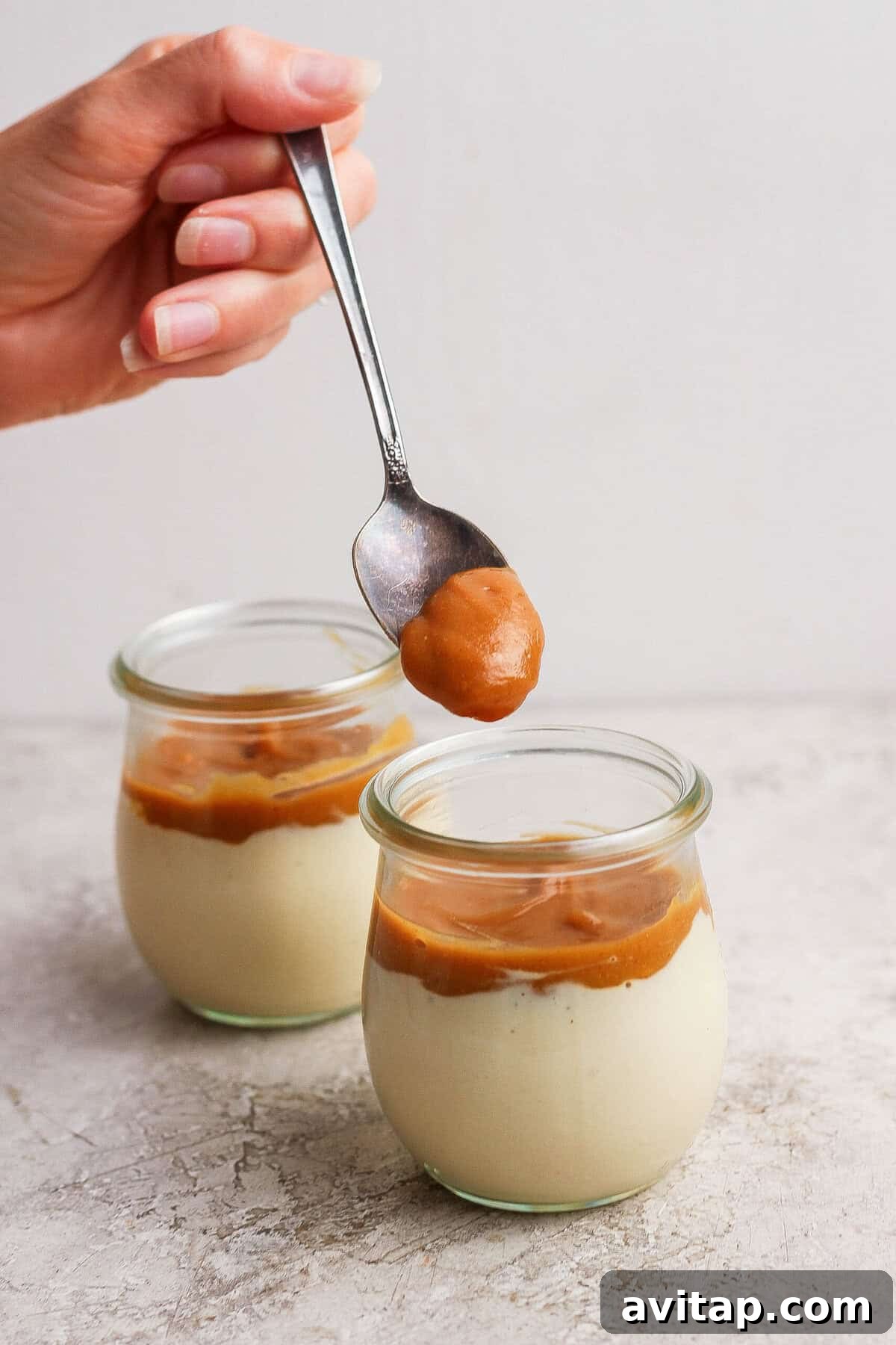 Maple peanut butter being spooned over the cottage cheese layer in individual dessert jars.